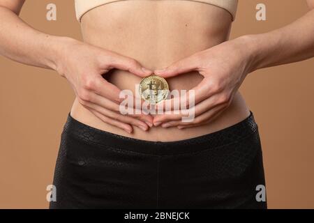 Nahaufnahme eines jungen Weibchens, das ein goldenes Bitcoin-Mädchen in den Händen auf dem Bauch hält Stockfoto