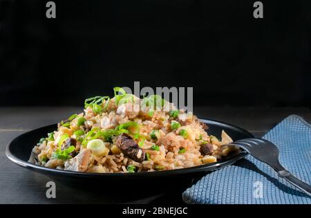 Chinesischer kantonesischer Bratreis mit Hühnchen, Erbsen und Schnittlauch auf schwarzem Hintergrund. Asiatisches Speisekonzept Stockfoto