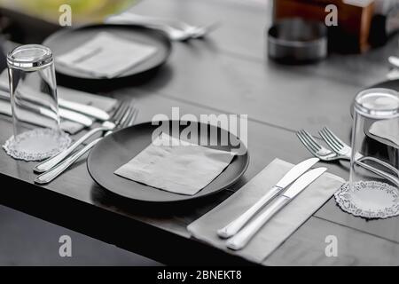 Nahaufnahme von Tellern und Gläsern auf dem Tisch mit Messern Und Gabeln auf Servietten unter den Lichtern Stockfoto