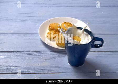 Cookie mit Milchspritzer in blauer Tasse auf hellblauem Holzhintergrund. Stockfoto
