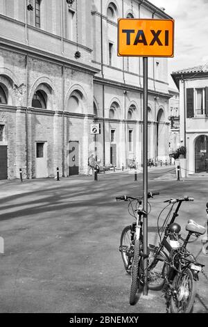 Gelbes Taxi-Schild mit geparkten Fahrrädern in der Nähe in Rimini, Italien. Teilweise Schwarzweiß Stockfoto