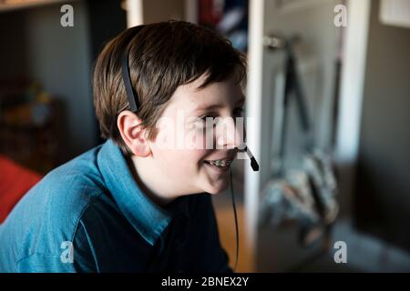 Seitenansicht von Smiling Teen mit Hosenträger mit Gaming-Headset Stockfoto