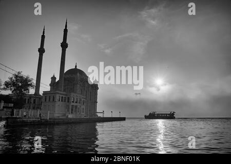 Ortakoy Moschee und Bosporus Brücke in Istanbul, Türkei. Dramatischer Himmel. Die Martyrs-Brücke vom 15. Juli im Nebel. Passagierboot auf dem Meer an einem Foggy Day Stockfoto