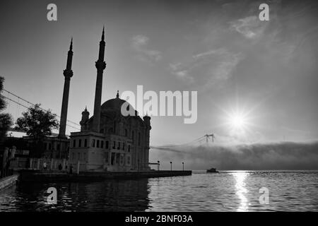 Ortakoy Moschee und Bosporus Brücke in Istanbul, Türkei. Dramatischer Himmel. Die Martyrs-Brücke vom 15. Juli im Nebel. Schnellboot auf dem Meer an einem Foggy Day Stockfoto