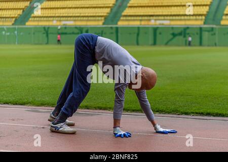 Ein alter Mann wird durch Nachahmung Schildkröten und Schlangen zu kriechen, um alle Gelenke im Körper zu verbessern und die Gesundheit auf einem Spielplatz zu verbessern gesehen, Stockfoto