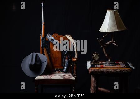 Hebel Aktion Gewehr, Revolver, Seil, Cowboy Hut, Uhr, Tisch, Lampe und ein Stuhl mit schwarzem Hintergrund, horizontal Stockfoto