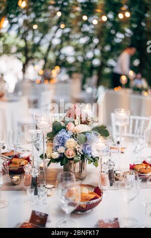 Empfang am Tisch für Hochzeitsessen. Blumenstrauß in einer Vase auf einem Tisch aus rosa und weißen Rosen und blauen Hortensien, mit der Nummer des Tisches auf dem Teller Stockfoto