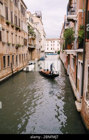 Italien Hochzeit in Venedig. Ein Gondolier rollt ein Brautpaar in einer klassischen Holzgondel entlang eines engen venezianischen Kanals. Weitwinkel, kleiner Kanal Ausgang zu Stockfoto