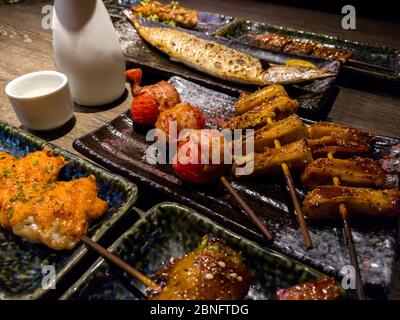Ein Set köstlicher traditioneller Spieße, die zum Abendessen gegrillt werden. Beliebte japanische Küche mit vielfältiger Auswahl im Restaurant. Appetitlich Japan Spießteller auf Holztabl Stockfoto