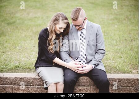 Pärchen sitzt, während sie die Hände zusammenhält und neben einem betet Rasenfläche Stockfoto