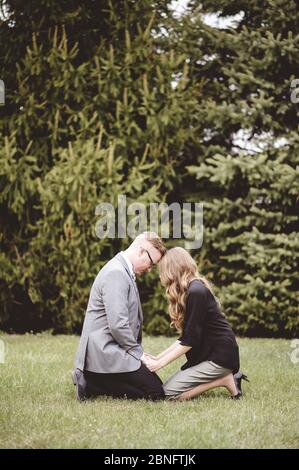 Ein Paar betet zusammen auf den Knien auf einem Gras Rasen mit Bäumen im Hintergrund Stockfoto