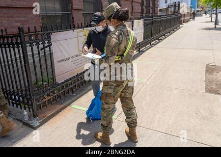 New York, Usa. Mai 2020. Ein Mitglied der US Army National Guard überprüft die Identität eines Mannes, bevor er ihm in einer Speisekammer inmitten der Coronavirus-Pandemie (Covid-19) im Stadtteil Queens in New York City Essen und andere wichtige Dinge gibt. Quelle: SOPA Images Limited/Alamy Live News Stockfoto