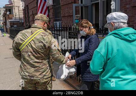 New York, Usa. Mai 2020. Eine Frau erhält Nahrung und andere wichtige Dinge von einem Mitglied der US Army National Guard in einer Speisekammer inmitten der Coronavirus-Pandemie (Covid-19) im Stadtteil Queens in New York City. Quelle: SOPA Images Limited/Alamy Live News Stockfoto