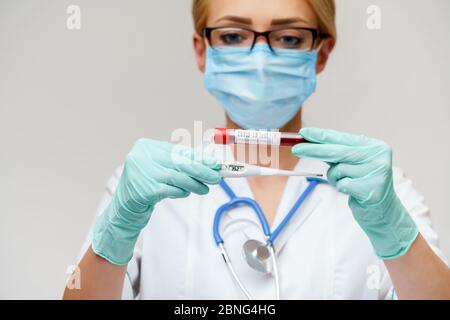 Arzt Krankenschwester Frau mit Schutzmaske und Handschuhe - hält elektronische Thermometer Stockfoto