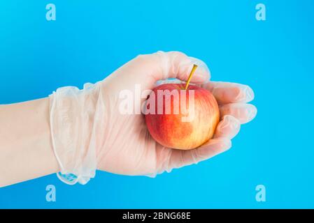 Hand in Gummihandschuh hält den roten Apfel. Konzeption der sicheren Lieferung Stockfoto