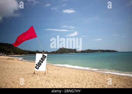 Konzept Quarantäne, Pandemie, Coronavirus, Reiseverbot. Tropischer Strand an einem sonnigen Tag ohne Menschen. Es gibt eine rote Flagge und ein Schild mit der Aufschrift geschlossen. Stockfoto