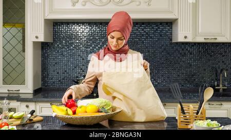 Pretty muslimische Frau in Hijab nimmt gekaufte Produkte aus großen Tasche für das Abendessen in der Küche Nahaufnahme Stockfoto
