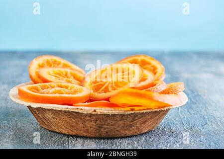 Scheiben getrockneter Orangen oder Mandarinen in einem Holzteller auf blauem Hintergrund. Vegetarismus und gesunde Ernährung. Kopierbereich Stockfoto