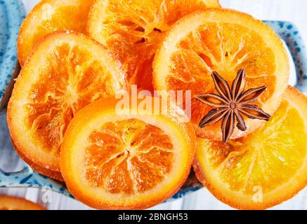 Scheiben getrockneter Orangen oder Mandarinen mit Anis und Zimt in einer blauen Schüssel auf hellem Hintergrund. Vegetarismus und gesunde Ernährung Stockfoto