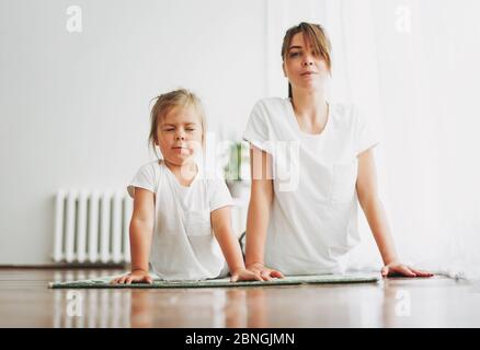 Mama und lustige kleine Tochter tun Yoga-Morgen-Übung zusammen im hellen Innenraum zu Hause Stockfoto