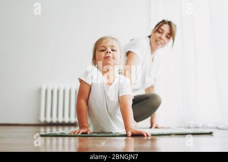 Glückliche Mutter und kleine Tochter tun Yoga-Morgen-Übung zusammen im hellen Inneren Haus Stockfoto