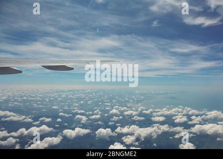 Luftbild vom Flugzeug aus. Fliegen über die Schicht der Wolken und Blick auf die Landschaft durch die Wolken. Weiches Sonnenlicht im Himmel. Stockfoto