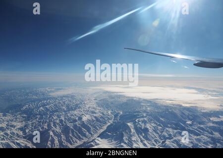 Grenzenlose fantastische Berge reichen unter seltenen weißen Wolken gegen riesigen blauen Himmel Blick aus dem Flugzeugfenster Stockfoto