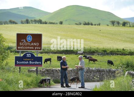 Zwei bäuerliche Nachbarn, ein Schotte (links) und der andere Engländer unterhalten sich an der England-Schottland-Grenze bei Kirk Yetholm. Stockfoto