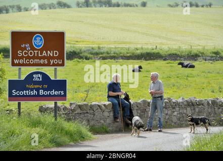 Zwei bäuerliche Nachbarn, ein Schotte (links) und der andere Engländer unterhalten sich an der England-Schottland-Grenze bei Kirk Yetholm. Stockfoto