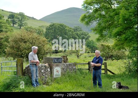 Zwei landwirtschaftliche Nachbarn, ein Schotte (rechts) und der andere Engländer unterhalten sich an der England-Schottland-Grenze in der Nähe von Kirk Yetholm, Schottland. Stockfoto