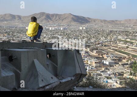 Junge sitzt auf zerstörten Tank auf den Hügeln über Kabul City in Afghanistan Stockfoto