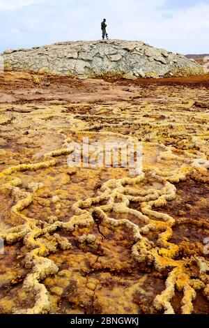 Bewaffneter Soldat in der Danakil Wüste mit Formationen, die durch Salzablagerungen, Winderosion, Wasser und schwefelhaltige Dämpfe verursacht werden. Dallol Gegend, Assale See, Afar Reg Stockfoto