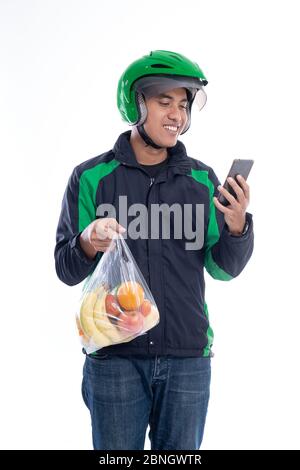 Lebensmittelzustellung. Kurier trägt Helm und Jacke Uniform hält Lebensmittel isoliert über weißem Hintergrund Stockfoto