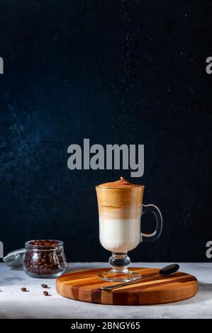 Iced Dalgona Kaffee mit Sifting Kakao auf hellgrau und dunklen Hintergrund. Trendy Cremigen Schlagsahne Kaffee. Südkoreanischer Kaltsommer-Drink. Stockfoto