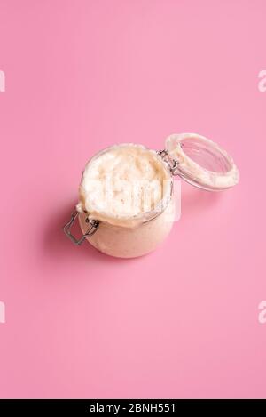 Fermentierter Sauerteig-Starter in einem Glasgefäß auf rosa nahtlosem Hintergrund. Glas selbstgemachten Sauerteig für die Brotherstellung. Mutterteig aus Weizenmehl. Stockfoto