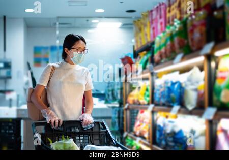 Asiatische Frau, die auf dem Markt Lebensmittel kauft, trägt Maske und Handschuhe, um die Ausbreitung von Virius während der Coronavirus-Pandemie zu verhindern Stockfoto