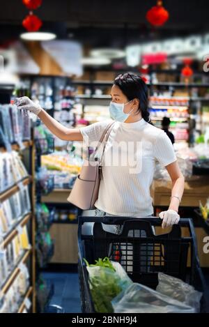 Asiatische Frau, die auf dem Markt Lebensmittel kauft, trägt Maske und Handschuhe, um die Ausbreitung des Virus während der Coronavirus-Pandemie zu verhindern Stockfoto