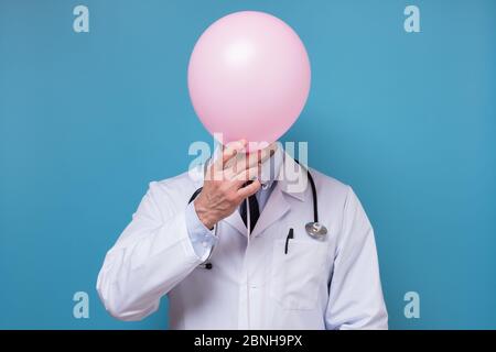 Doktor in weißem Mantel mit Stethoskop versteckt sich hinter einem Ballon Stockfoto