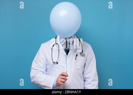 Doktor in weißem Mantel mit Stethoskop versteckt sich hinter einem Ballon Stockfoto