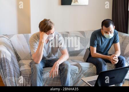 Zwei gestresste multi ethnischen Männer mit Maske als Freunde suchen depressiv während Videoanrufe zu Hause unter Quarantäne Stockfoto