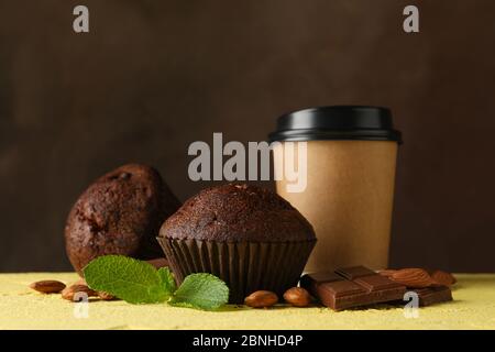 Zusammensetzung mit leckeren Muffins und Pappbecher auf gelbem Tisch Stockfoto