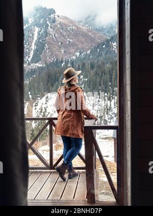 Frau im Hut mit beim Holzhaus im Bergort im Winter Stockfoto