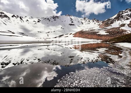 Schöne Landschaft des Titov-Sees mit Spiegelung der schneebedeckten Berge und bewölktem Himmel in Tien Shan Tal des südlichen Kasachstan Stockfoto