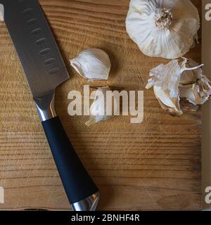 Draufsicht auf ein Messer und Knoblauchzwiebeln und Nelken Auf einem hölzernen Schneidebrett Stockfoto