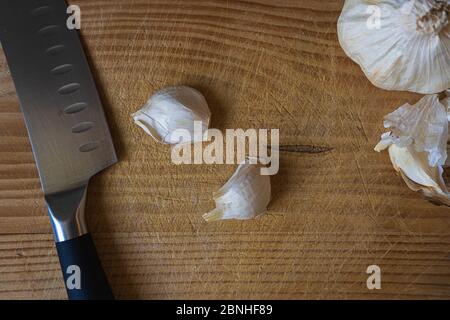 Draufsicht auf ein Messer und Knoblauchzwiebeln und Nelken Auf einem hölzernen Schneidebrett Stockfoto