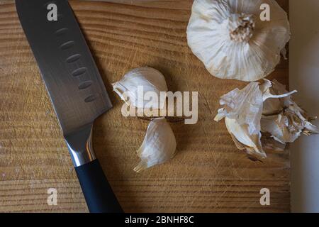 Draufsicht auf ein Messer und Knoblauchzwiebeln und Nelken Auf einem hölzernen Schneidebrett Stockfoto