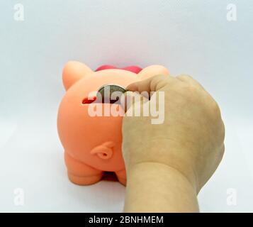 Hand einer Person, die eine Münze in ein Plastikschwein in einem weißen Hintergrund einführt Stockfoto