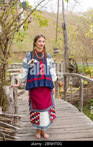 Ein Mädchen in Nationalkleidung läuft durch eine alte Brücke. Alte Kleidung. Retro-Inszenierung eines alten Ritus. Schönes Kleid und Rock auf einer Frau. Perlen Stockfoto