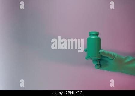 Schöne Hand halten Grüne Flasche für Pillen in der Farbe Licht. Wunderschönes altes Minimal in Neonlicht. Minimalistisches Retro-Konzept. Hintergrundmuster Stockfoto
