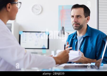 Reifer Mann, der mit seiner Ärztin über seine Gesundheit spricht, während sie im Büro am Tisch sitzen Stockfoto